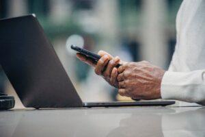 Person using smartphone near a laptop outdoors.